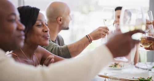 Group of friends saying cheers while lifting their wine glasses to share a toast during lunch around