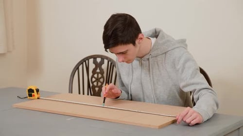 Boy Marking Precise Measurements on Wooden Board Using Pencil Male Student Preparing Design Plan for