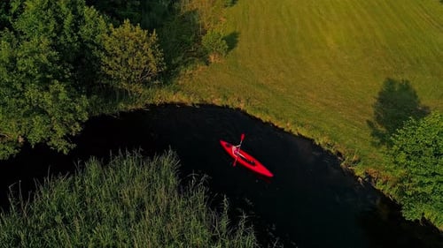 Aerial footage of a person riding a kayak/canoe down a river, surrounded by lush greenery