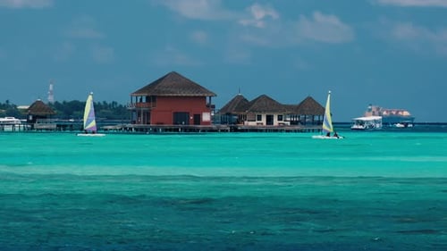 Maledivische Meereslandschaft mit türkisfarbenem Wasser, Gebäuden des Resorts und Segelbooten