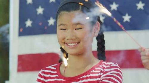 Smiling Girl Holding Sparkler in Front of US Flag