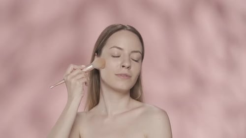 Seminude Woman Uses a Makeup Brush in the Studio on a Pink Background Close Up A Woman Does