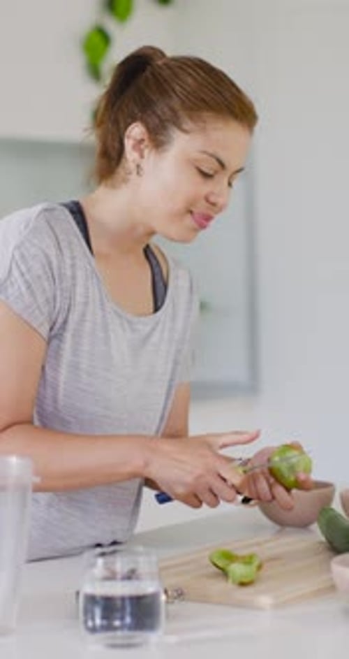Vertical video: African American woman peeling fruit in kitchen using small knife for snack prep