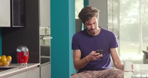 Man Using Phone and Drinking Coffee in Kitchen