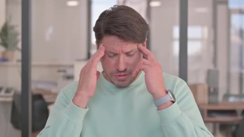 Man rubbing forehead with headache in workplace