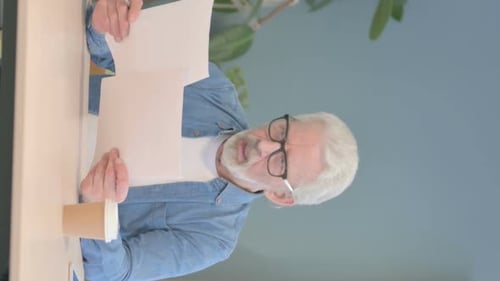 Senior Adult Reads Document at Desk