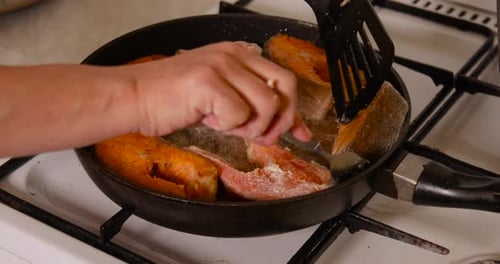 Moving and turning frying salmon fish in a hot pan with sizzling oil