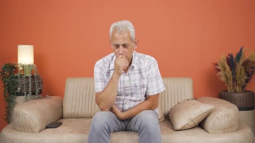 Man Sitting on Couch Coughing and Touching Stomach