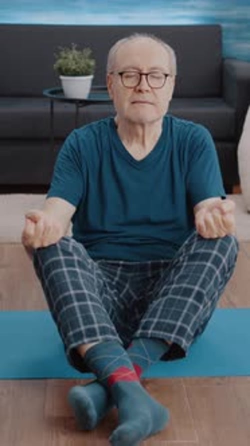 Mature Man Meditating at Home on Yoga Mat