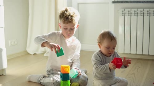 Zwei Kinder bauen einen Turm aus Blöcken und sitzen auf dem Boden in einem sonnigen Schlafzimmer
