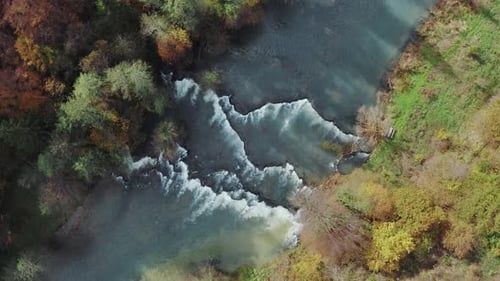 Top-down view of a mountain river with rapids surrounded by thick forest.