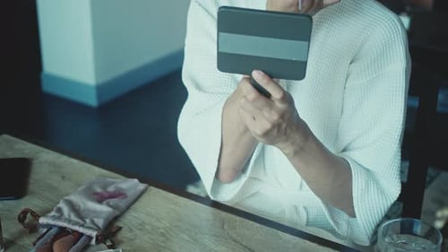 Person Applies Makeup Using Brush and Mirror