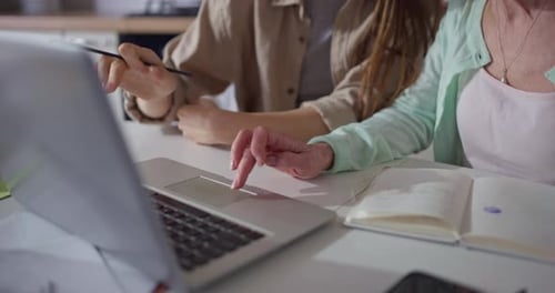 Daughter Helps Her Mature Mother Use Laptop and Gives Advice While Working at Table in Cozy Kitchen