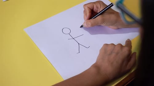 Female Hands Draw Two Human Stick Holding Each Other On White Sheet. High Angle