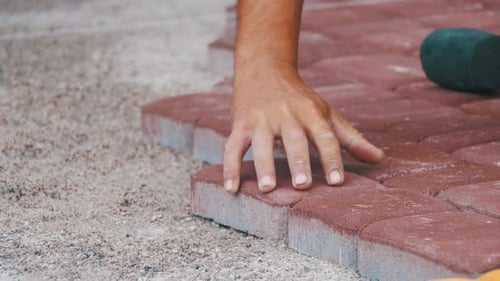 Hands Laying Red Brick Pavers on Surface