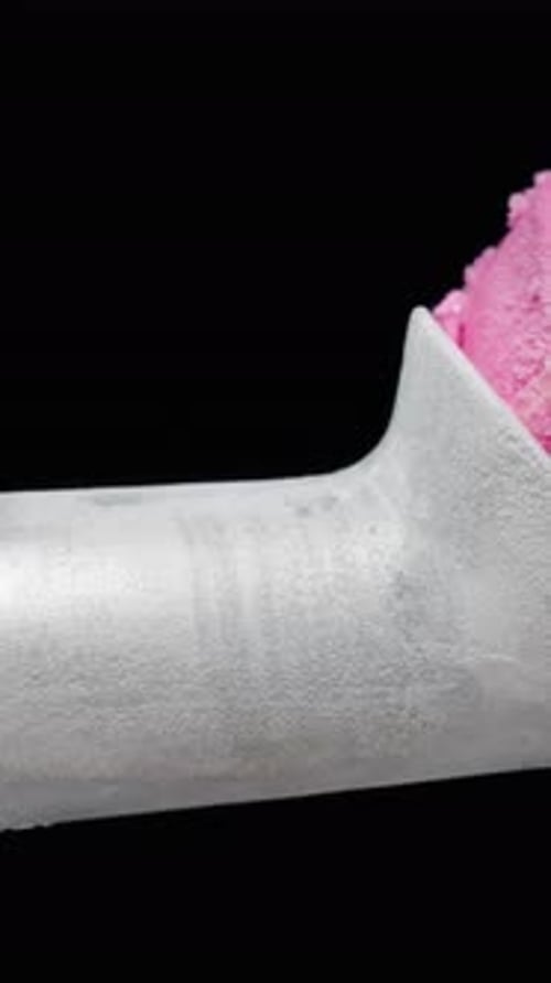 Vertical video. A frosted metal ice cream scoop and a pink ice cream ball placed in it, slider shot.