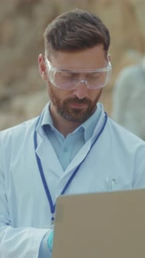 Man in Lab Coat and Goggles Writing Outdoors