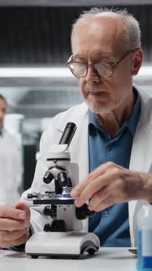 Senior man looks through microscope in lab setting