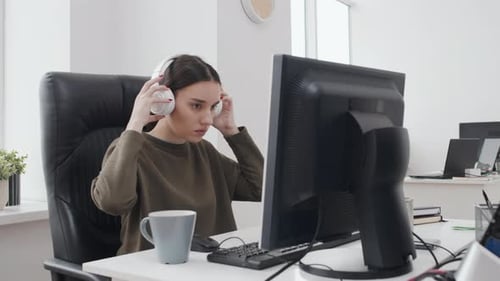 Young Woman Putting On Headphones At Work