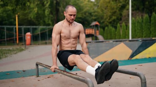 Muskulöser Mann macht Dips auf Parallelbars in einem Park