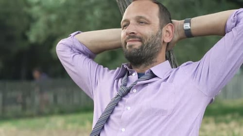 Young Businessman Stretching Arms and Relaxing on Grass in Park 30s