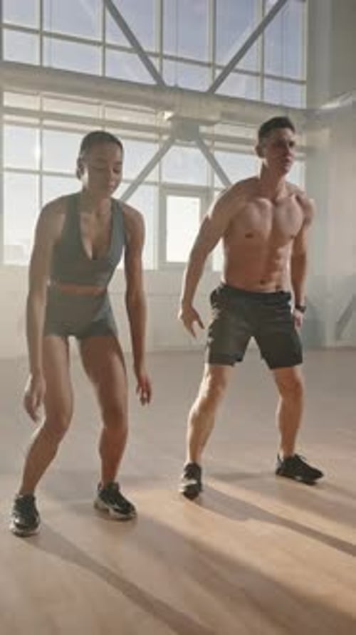 Determined Athletic Young Man and Woman Doing Jumping Jack or Jumping Squats Indoors Slow Motion