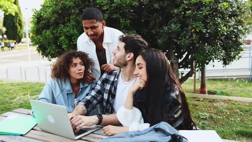 Students of different ethnicities working together on a laptop in an outdoor study session