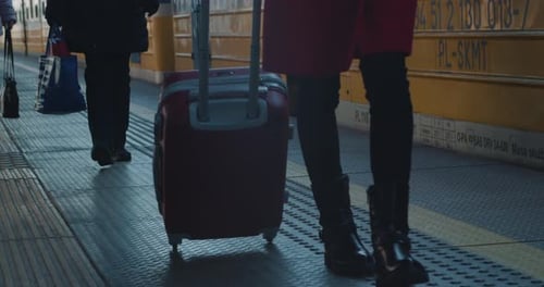 Young Girl with Luggage Walks Along a Departing Train at the Railway Station