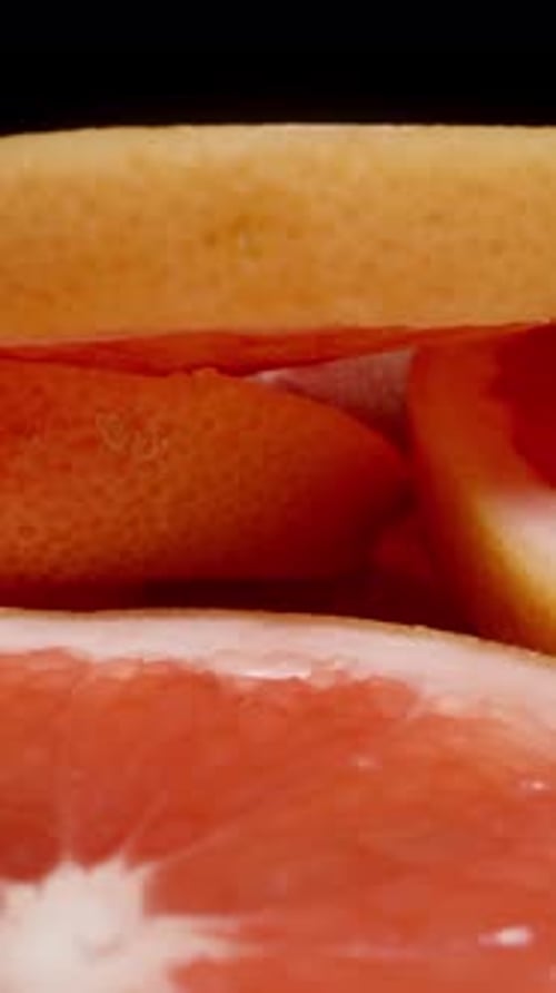 Vertikal. Die Hand nimmt Grapefruitscheiben vom Tisch auf, während sie sich auf sie zubewegt.