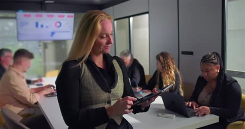 Businesswoman using digital tablet while team collaborates in background during office