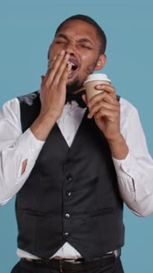 Vertical Video Hotel Concierge Staff Drinks Coffee While He is Yawning and Feeling Tired