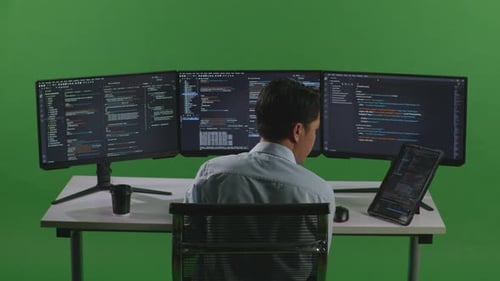 Asian Man Working With Tablet While Write Code With Multiple Computer Screens In Green Screen