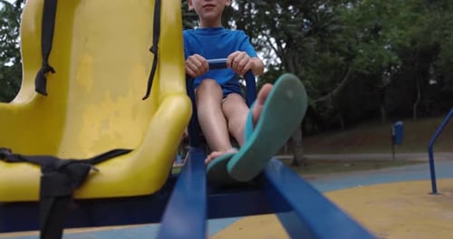 Boy going up and down on teeter-totter outside on summer day