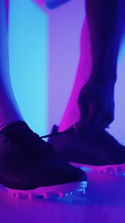 Image rapprochée d'un joueur de football attachant les lacets de crampons avec des néons violets et bleus vibrants