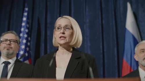 Woman Speaks at Podium with Flags in Background