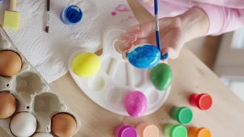 Woman painting Easter egg at home with pastel paints