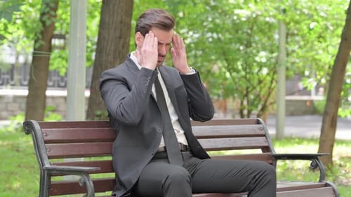 Tired Young Businessman Sitting Outdoor with Headache