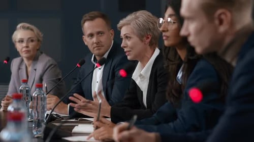Business professionals at conference table speaking into microphone