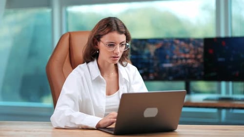 Businesswoman Working on Notebook in Modern Office with Glass Background and Computer Screen