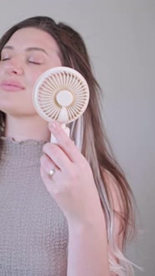 Woman Cooling Off with Portable Fan indoors