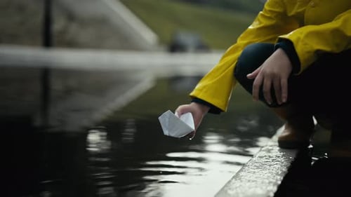 Child Plays with Paper Boat in Waterway