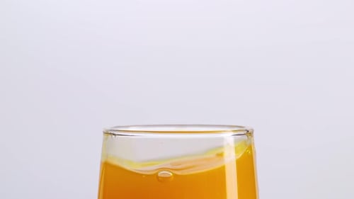 Close Up Of Ice Cube Falling In A Glass Of Orange Juice On The Light White Screen Background