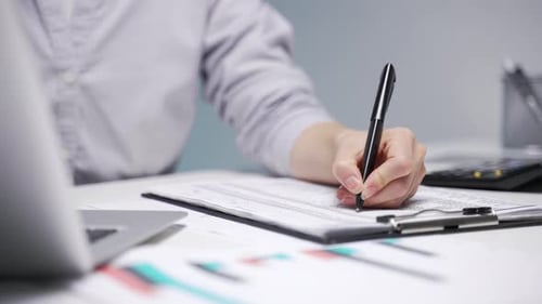 Close up of a female hand filling out documents with a pen at desk at workplace in a modern business