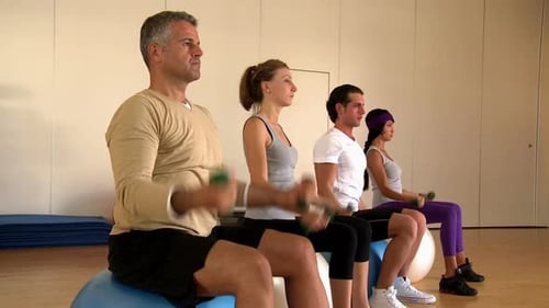 Smiling young people lifting dumbbells at gym with instructor leading workout