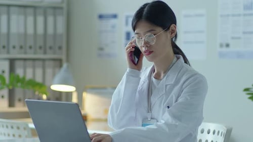 Doctor on Phone Using Laptop in Office