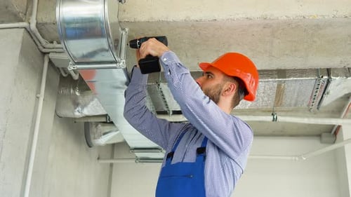 Man Installs Ventilation Ductwork with Power Drill