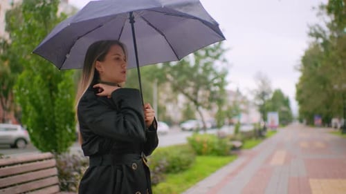 Lady in Black Trench Coat Holding Umbrella Standing on City Sidewalk