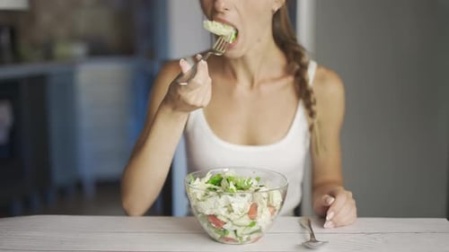 Woman Eating Fresh Salad at Kitchen Table