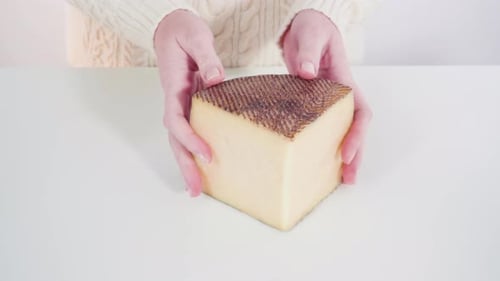 Woman Holds Wedge of Rustic Cheese on Table