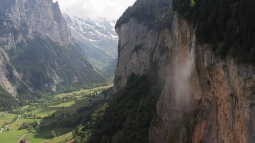 Aerial dolly of waterfall on mountainside to beautiful green valley
